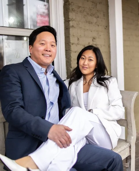 Owners Alex and Sora wearing business attire sitting together on a bench for the about us page.