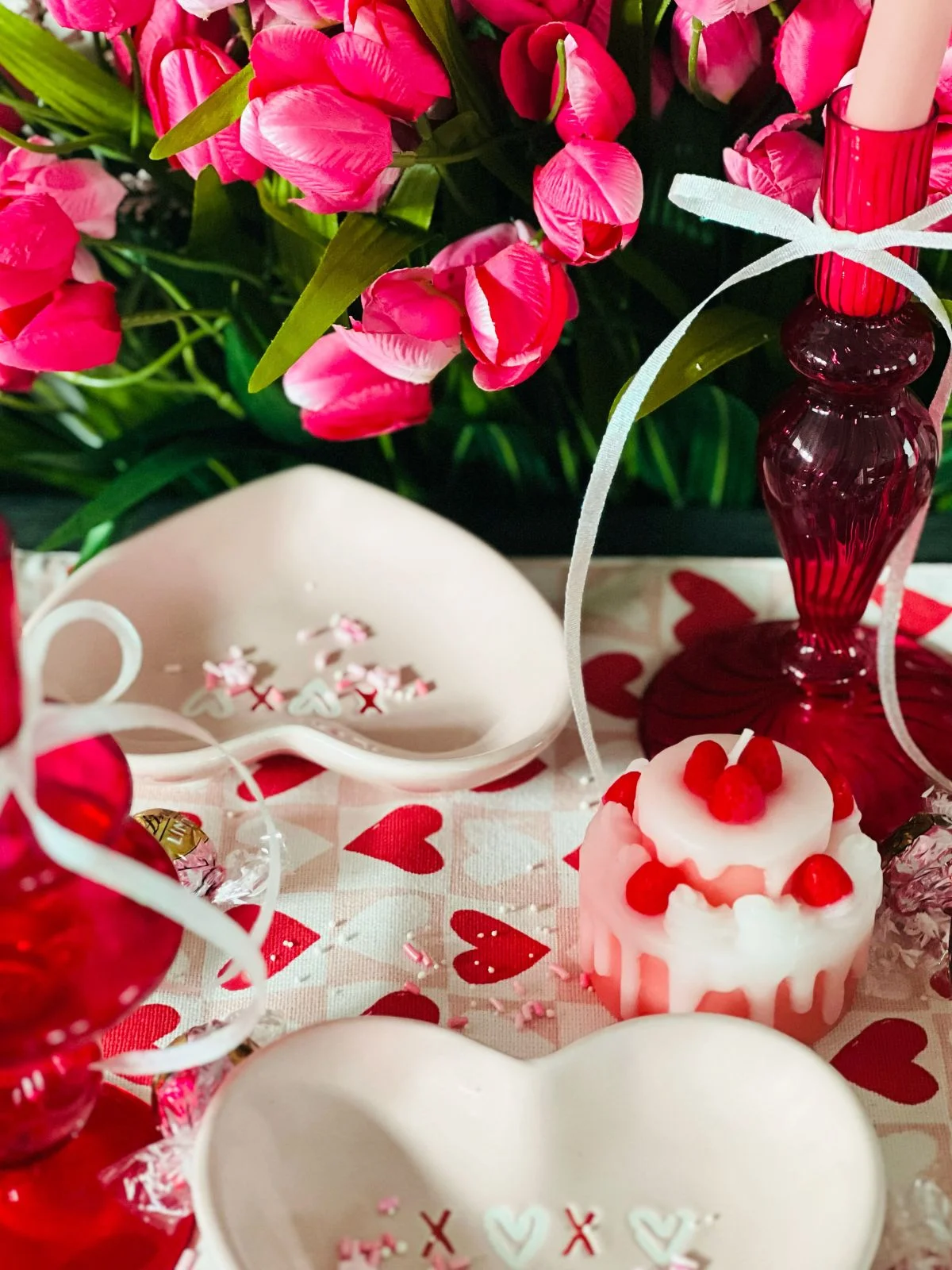 A vibrant setup for valentine's day featuring pink tulips, heart-shaped decorations, and a red candle with matching glassware.