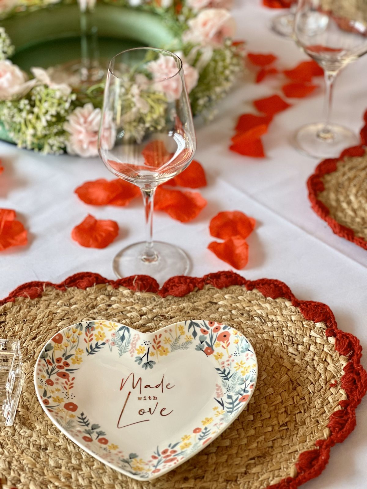 A decorated table setting with a heart-shaped plate, wine glasses, and rose petals.