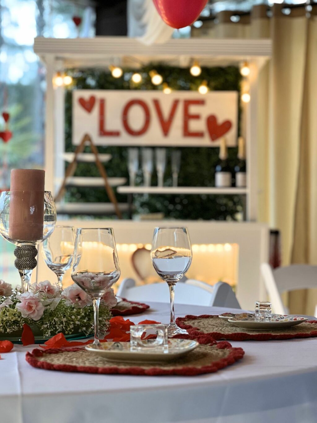 Romantic table setting for two with "love" sign and heart-shaped balloon in background by White Cloud event decorators in Atlanta.