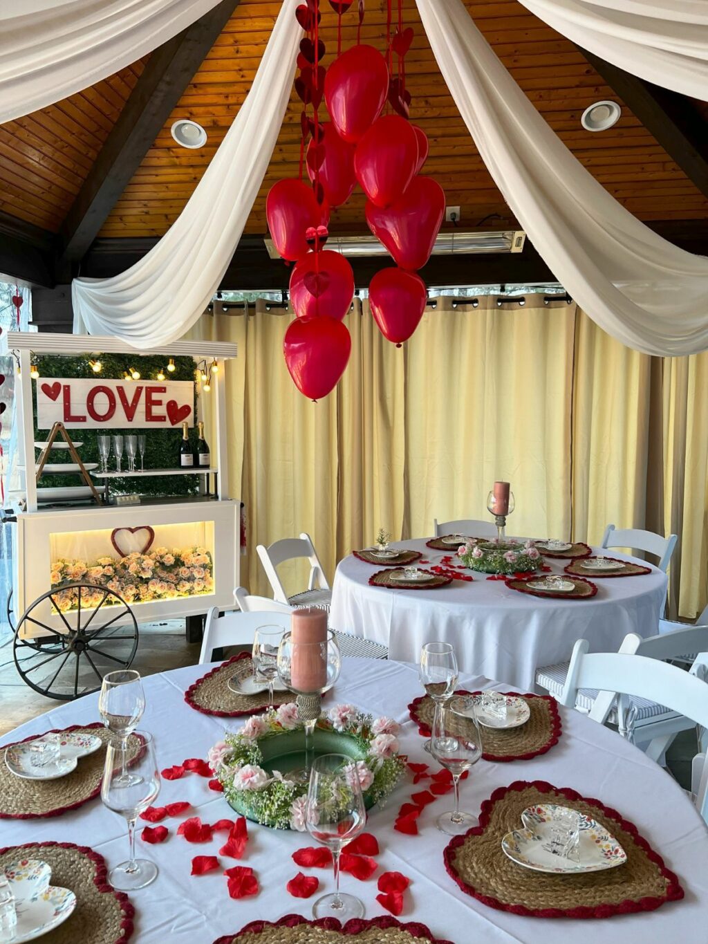 Valentine's day themed event setup with red heart balloons, 'love' sign, and decorated dining tables.