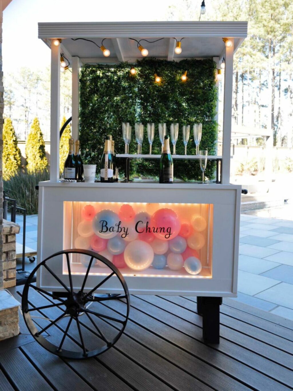 Custom cart decorated with a "baby chung" sign, champagne bottles, and colorful balloons, set up outdoors for event rentals.