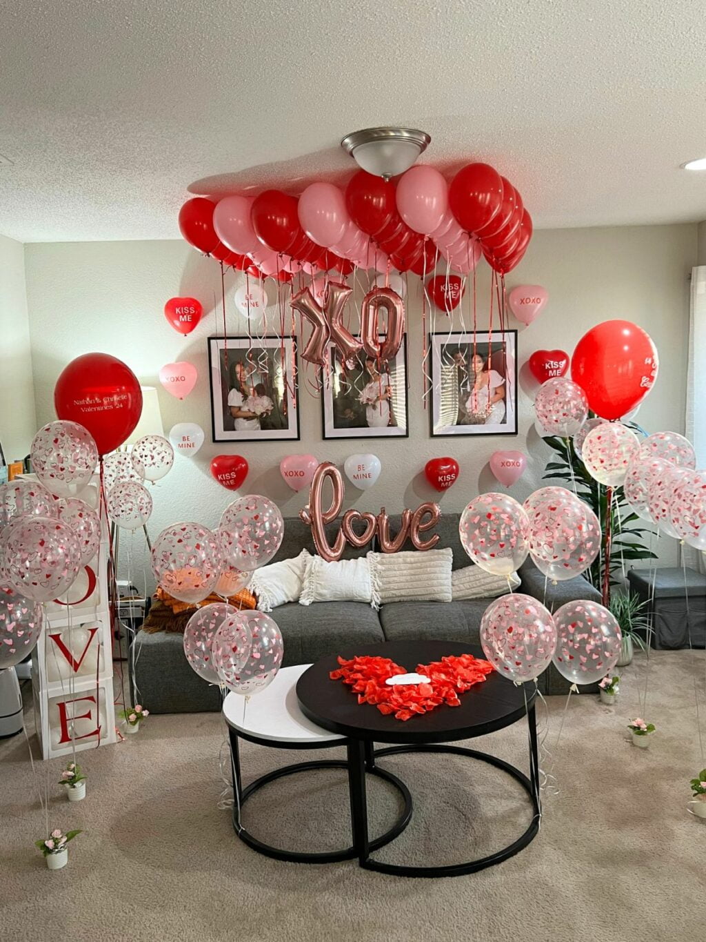 A valentine's day themed room decorated with red and pink balloons, "xo" and "love" signs, and rose petals.