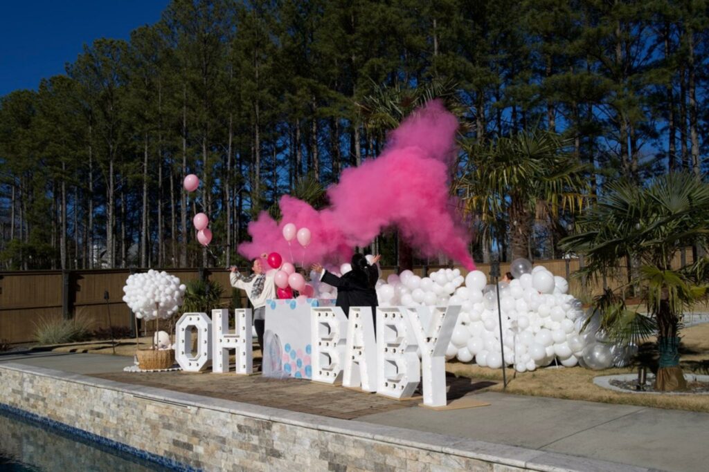 Gender reveal party with a pink smoke display indicating a baby girl with marquee letters for event rentals.