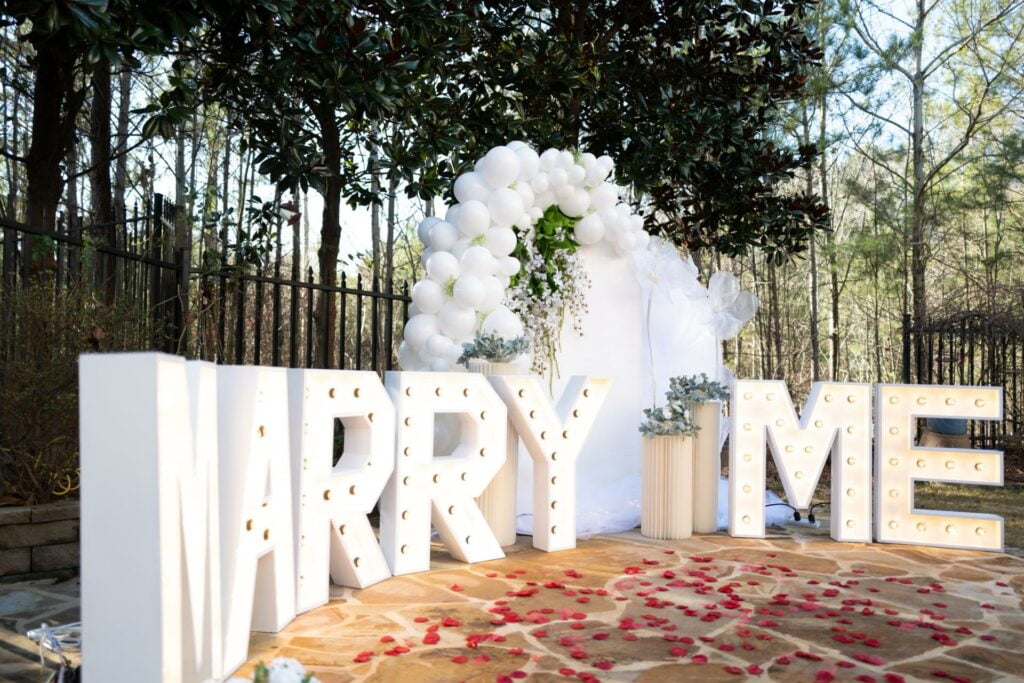 Outdoor marriage proposal setup with large "marry me" letters and a floral backdrop - contact White Cloud Decor for your upcoming proposal.